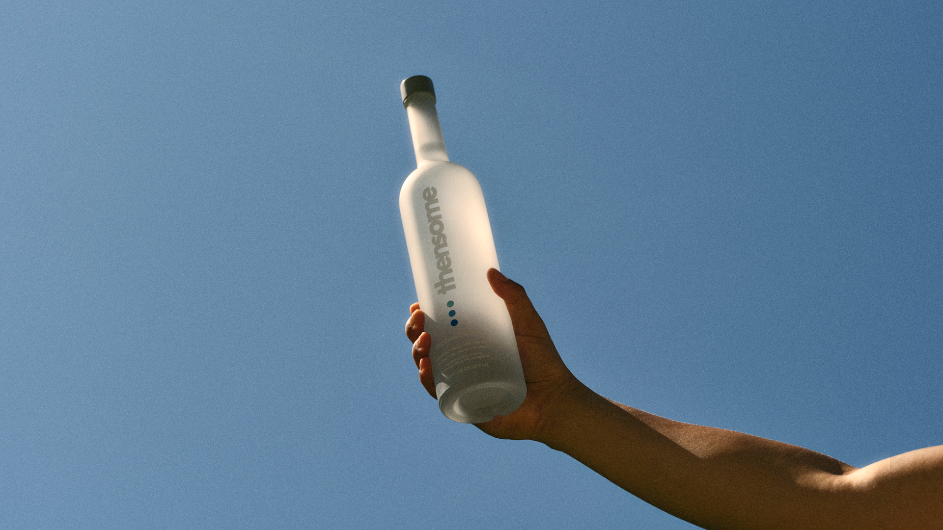 Man holding Thensome bottle in front of a blue sky